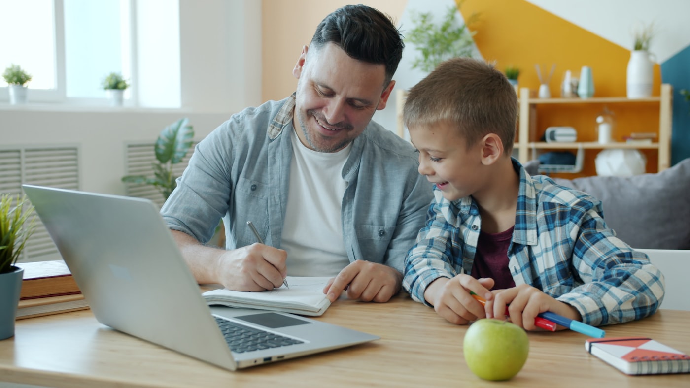 A parent and child sitting together at a kitchen table working through homework, soft afternoon light, hands on a notebook